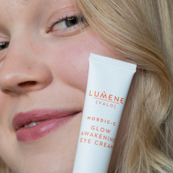 Rozświetlający krem pod oczy Lumene Nordic-C w białej tubce, trzymany blisko twarzy kobiety, widoczne logo.