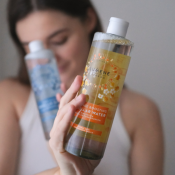 Lumene Kirkas Rozświetlająca woda micelarna z maliną moroszką, butelka z żółtymi płatkami w dłoni, obok niebieska.