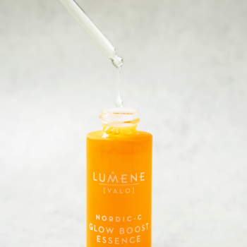 Pomarańczowa rozświetlająca esencja Lumene Nordic-C, kropla spływa z pipety, na jasnym tle.
