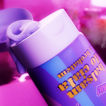 Zbliżenie na rozświetlający balsam do ciała Fluff Born to Party w fioletowo-niebieskiej tubce, z boku wydobywa się różowy krem.