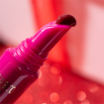 Kropla ciemnoróżowego Catrice peptide tint do ust na fuksjowym aplikatorze tubki, rozmyte czerwone tło.