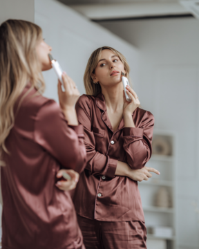 Kobieta w satynowej piżamie używa białego urządzenia Beautifly Scrub Slim PRO do peelingu kawitacyjnego twarzy przed lustrem.