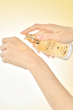 Ręka aplikuje rozświetlające serum d'Alba Vita Toning z białą truflą z złotej butelki na dłoń.