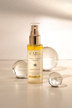 d'Alba White Truffle First Spray Serum, nawilżająco-rozświetlające, w złotej butelce z pompką, wśród szklanych kul.