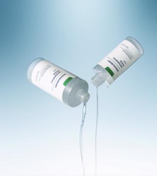 Dwie transparentne butelki Bioderma Sensibio H2O, z których wylewa się płyn, na jasnoniebieskim tle.