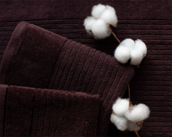 Ciemnobrązowe, złożone ręczniki bawełniane z prążkowaną fakturą, ozdobione białymi bawełnianymi kwiatami.