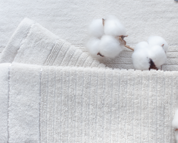 Zbliżenie na puszyste białe kulki bawełny ułożone na złożonej, prążkowanej tkaninie bawełnianej. Widok z góry.