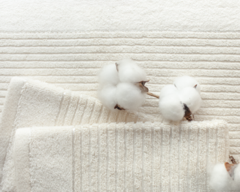 Trzy puszyste kłębki bawełny leżące na miękkiej, białej, prążkowanej tkaninie frotte, ukazując naturalną teksturę.