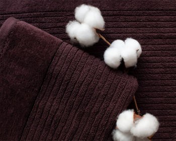 Trzy białe kłęby naturalnej bawełny na ciemnobrązowym, prążkowanym materiale, z widocznym złożeniem.