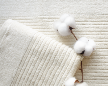 Naturalny, kremowy ręcznik bawełniany o prążkowanej teksturze, złożony, obok gałązki białej bawełny.