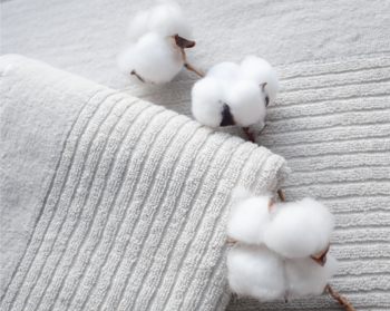 Naturalne puszyste kwiaty bawełny ułożone na jasnym, prążkowanym materiale tekstylnym, z bliska, widok z góry.
