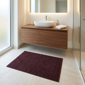 Ciemnofioletowy, prostokątny dywanik łazienkowy z wyraźnym brzegiem, leżący na jasnej podłodze w nowoczesnej łazience.