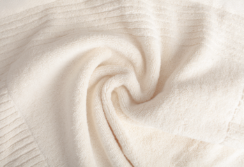 Zbliżenie na miękki, kremowy materiał, prawdopodobnie kaszmirowego swetra, z delikatnymi falami i prążkowanym brzegiem.