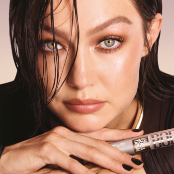 Kobieta z intensywnym makijażem oczu trzyma srebrny tusz Maybelline Lash Sensational pogrubiający rzęsy.