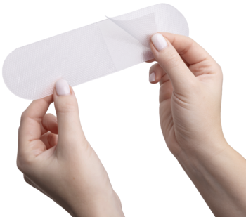 Dłonie odklejające biały, owalny plaster silikonowy Frida Mom na bliznę po cesarce, widok z bliska.