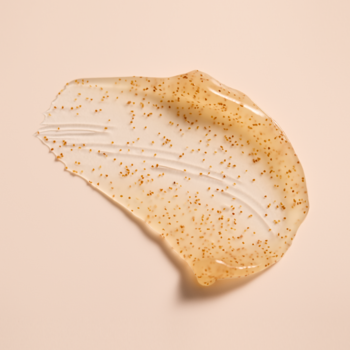 Zbliżenie: peeling OPI Nature Strong z brązowymi drobinkami, złoty żel rozmazany na beżowym tle.