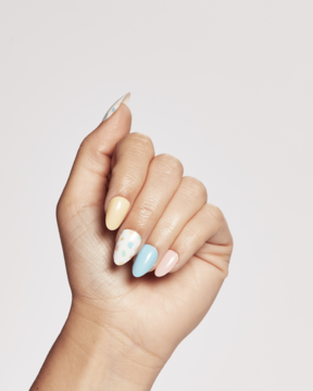 Ardell Nail Addict Nail Strips: dłoń z pastelowymi, wzorzystymi naklejkami na migdałowych paznokciach. Jasne tło.