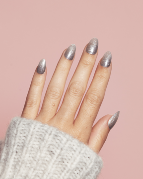 Ardell Nail Addict Nail Strips: dłoń z długimi, srebrnymi, brokatowymi paznokciami w kształcie migdała, widok z góry.