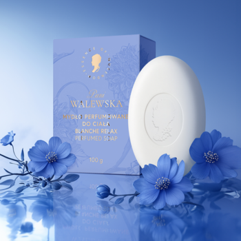 Białe owalne perfumowane mydło Pani Walewska BLANCHE RELAX z logo, niebieskie pudełko i kwiaty na lustrzanej powierzchni.