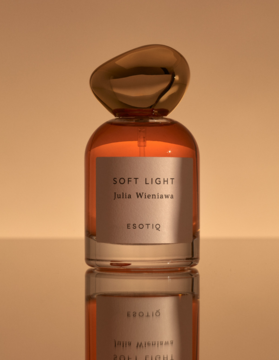 Eleganckie perfumy Soft Light Esotiq w butelce z pomarańczowym płynem i złotą nakrętką, na lustrzanej podstawie.
