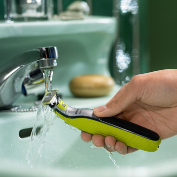 Zielono-czarny Philips OneBlade płukany pod bieżącą wodą w umywalce, podkreśla wodoodporność urządzenia.