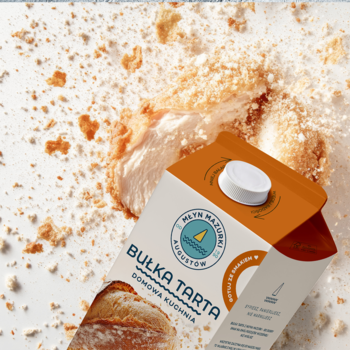 Karton bułki tartej Młyn Mazurski Augustów, pomarańczowo-biały, na tle panierowanego kurczaka i rozsypanych okruchów.