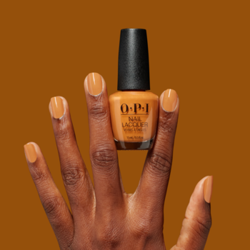 Pomarańczowy lakier do paznokci OPI Nail Lacquer, trzymany przez dłoń z pomalowanymi paznokciami, na tle w tym samym kolorze.