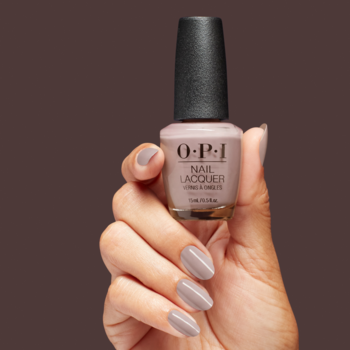 Ręka trzyma butelkę lakieru O.P.I. Nail Lacquer w kremowym odcieniu jasnego beżu/taupe, z paznokciami pomalowanymi identycznie.