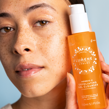 Kobieta trzyma pomarańczowy złuszczający żel do mycia Lumene Nordic-C 150ml blisko twarzy, widok z przodu.