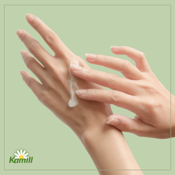 Kamill, krem do rąk z organicznym rumiankiem. Dłonie wmasowują biały balsam w skórę na zielonym tle.