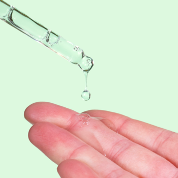 Serum z niacynamidem 10% i Zinc PCA. Transparentna kropla spływa z pipety na dłoń, jasne tło.