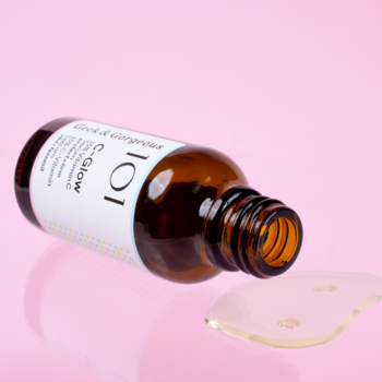 C-Glow serum z 15% witaminą C, brązowa butelka leżąca na boku, wylewający się płyn na różowym tle.