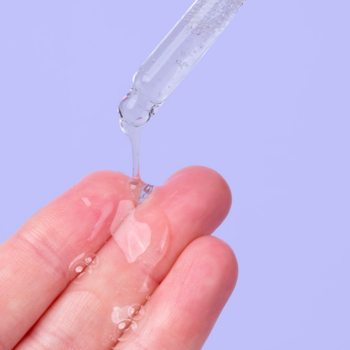 Krople nawilżającego, żelowego serum Stress Less z aplikatora, delikatnie spływające na palce, na fioletowym tle.