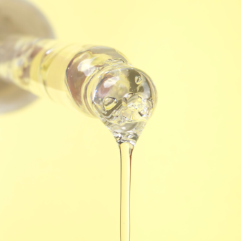 Lekkie serum z 2% kwasem salicylowym spływa z szyjki szklanej butelki, przezroczysty płyn na żółtym tle.