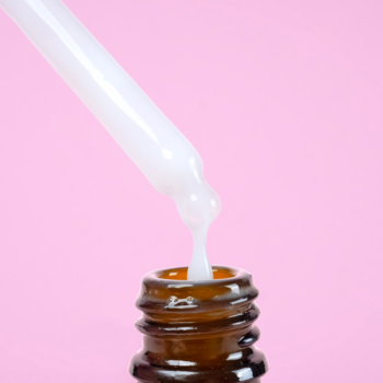 Zbliżenie na biały zakraplacz, który dozuje kremowe serum Power Peptides do ciemnej szklanej butelki na różowym tle.