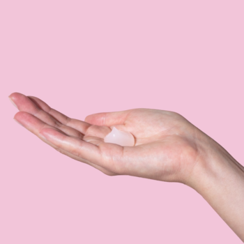 Otwarta dłoń z perłowym żelem do mycia twarzy z pantenolem, na tle w kolorze pudrowego różu.