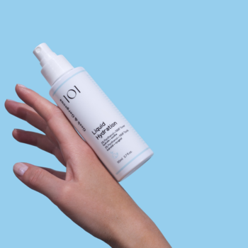 Tonik Liquid Hydration Sensumare 101 z pantenolem w białej butelce, trzymany w dłoni na błękitnym tle.