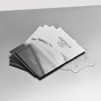 Stos białych saszetek maski Skin1004 Madagascar Centella Tone Brightening Glow; obok wylana rozświetlająca esencja.