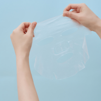 SKIN1004 Hyalu-Cica Hydrating Mask. Dłonie rozciągają przezroczystą maskę w płachcie z kwasem hialuronowym.