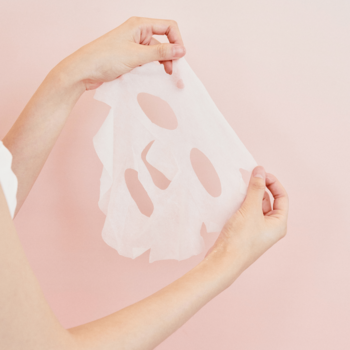 SKIN1004 Madagascar Centella Poremizing Clarifying Mask, biała maska w płachcie trzymana w dłoniach, różowe tło.