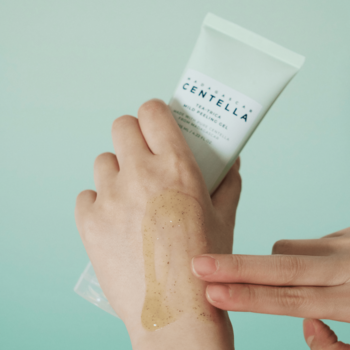 Dłoń prezentuje SKIN1004 Tea-Trica Mild Peeling Gel w jasnozielonej tubce i beżowy żel z drobinkami na skórze.