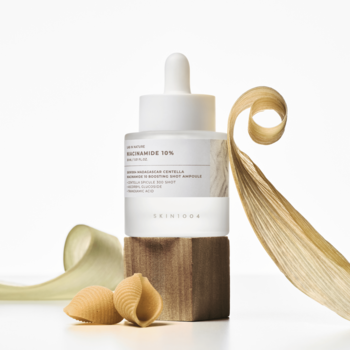 Biała ampułka SKIN1004 Niacinamide 10% do wyrównywania kolorytu, na drewnianym bloku z makaronem i wstążkami.