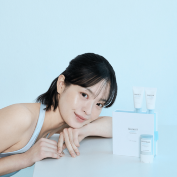 Uśmiechnięta kobieta z zestawem SKIN1004 Hyalu-Cica Sunsational Kit: białe serum i sztyft SPF na błękitnym tle.