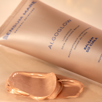 Sensum Mare Algoglow balsam rozświetlający w złotej tubce i lśniąca próbka kremu na stole.