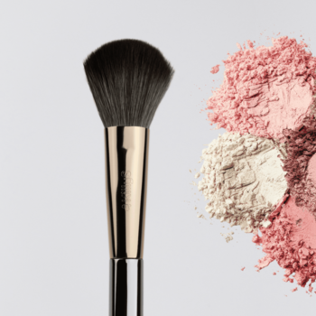 KillyS Beauty Icon pędzel do pudru i rozświetlacza z syntetycznym włosiem, obok stosy różowych i beżowych pudrów.