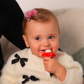 Zbliżenie na roześmiane niemowlę, które żuje czerwony, silikonowy gryzak grzybek RaZbaby na ząbkowanie.