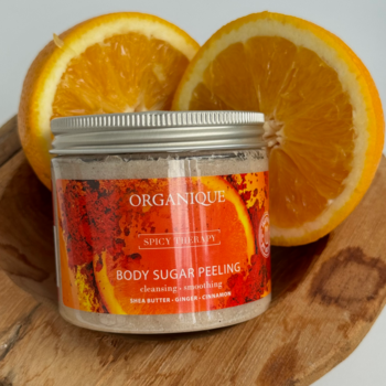 Organique peeling cukrowy pomarańcza i przyprawy, w szklanym słoiku, obok świeże połówki pomarańczy na drewnie.