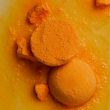 Zbliżenie na dwie pomarańczowe kule do kąpieli z olejkami o orientalnym zapachu, otoczone żółtą pianą.