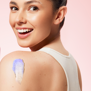 beBIO Naturalny peeling do ciała honey & fig: uśmiechnięta kobieta prezentuje fioletowo-biały peeling na ramieniu.