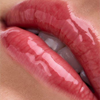 Zbliżenie na błyszczące różowe usta z Catrice Peptide Bliss Glossy Lip Balm 030 Dew Not Disturb, widać białe zęby.